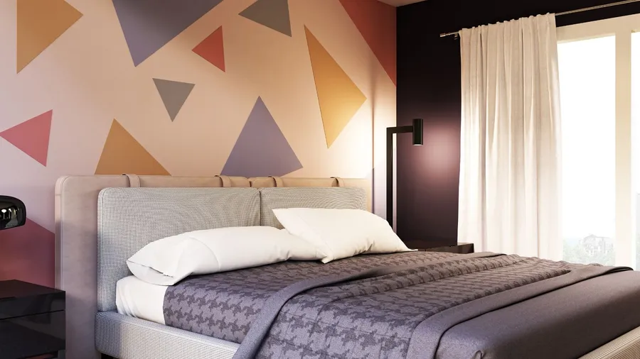 A bedroom interior with a cozy bed, white curtains, a lamp, and an geometric patterned colorful accent wall.