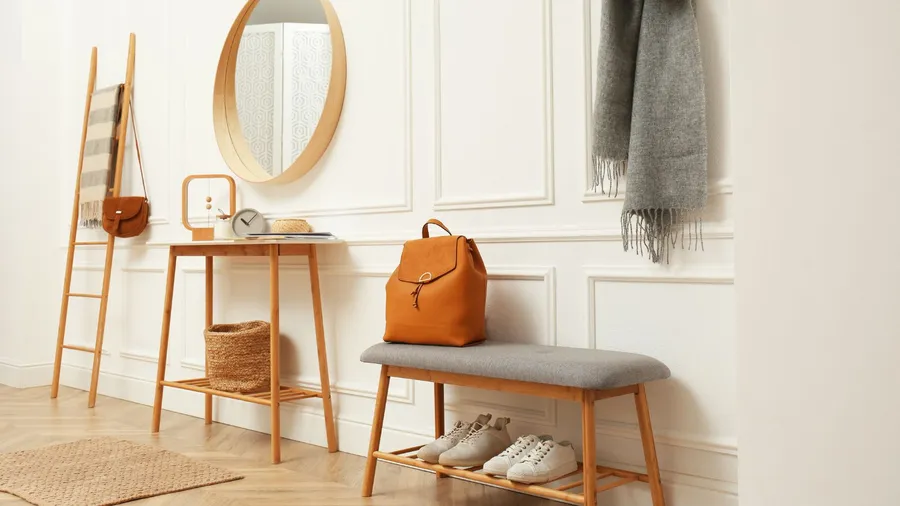 An organized entryway with a mirror, luggage, and shoes placed on a bench.