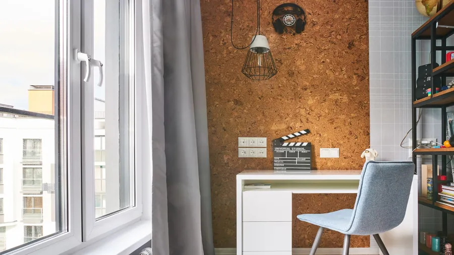 A home office interior with a white table and chair in front of a corkscrew wall, shelf, and blackout curtains on the window.