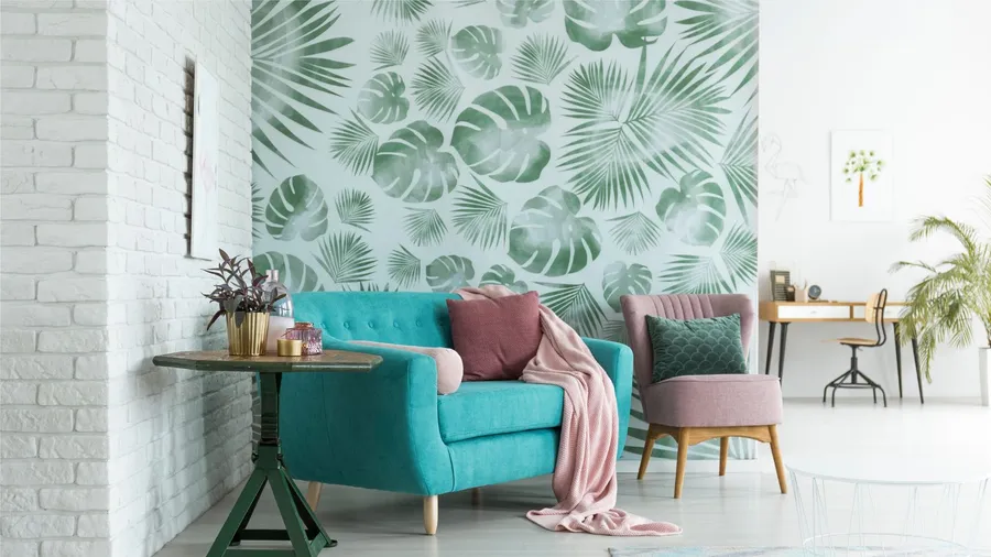 A modern living room with a teal sofa, pink chair, tropical leaf wallpaper, and a side table with plants.