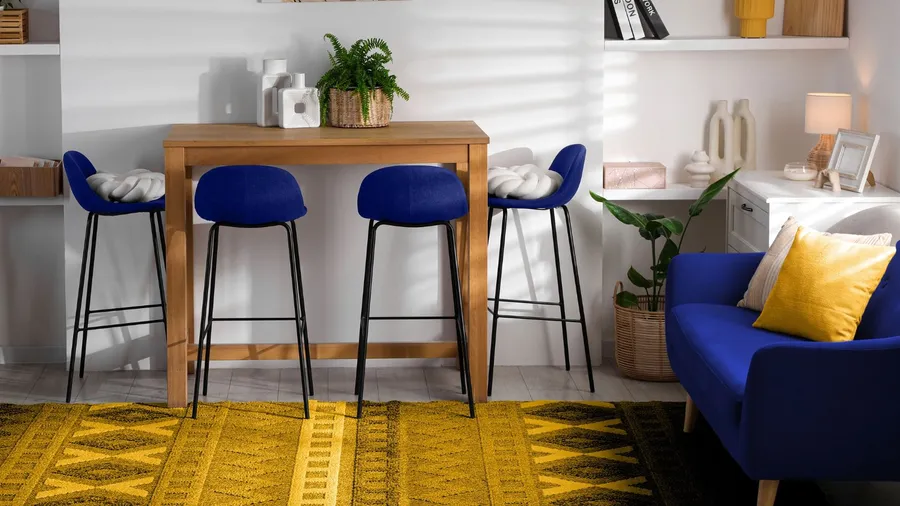 A cozy nook with wooden table and chair, sofa with throw pillows, and a patterned mustard rug.