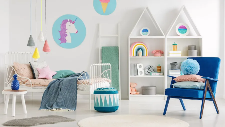 A stylish kids bedroom with a bed, pouf, armchair, white shelf with decor pieces, and a ladder with a towel leaning on the wall.