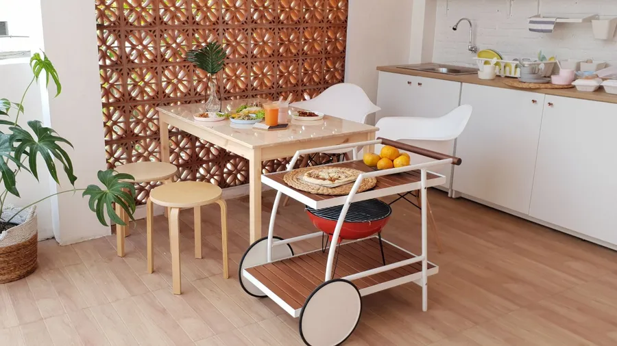 A kitchen interior with white cabinets, wooden dining table, and a kitchen rolling cart with a grill and food items.