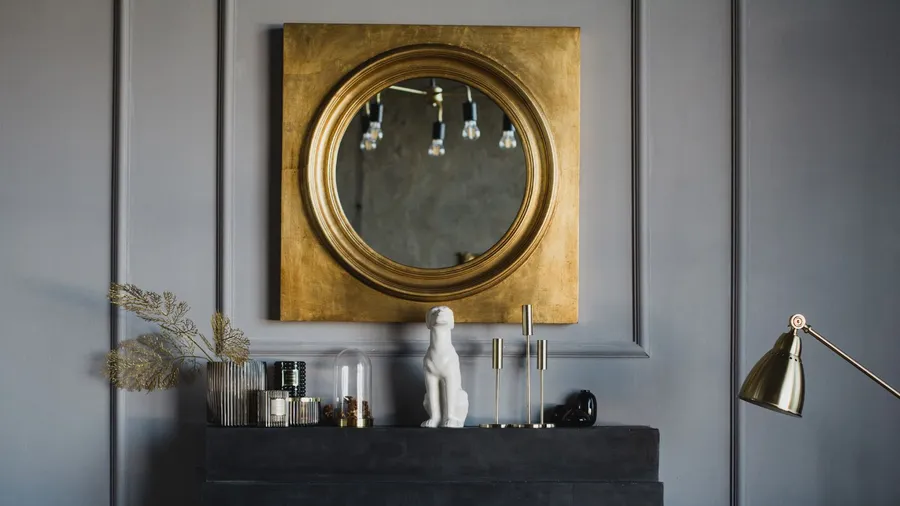 A statement mirror with gold frame hanging above the fireplace mantel with decor accents on it.
