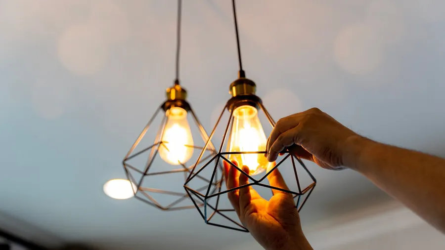 A person fixing LED bulb in a pendant hanging from the ceiling.