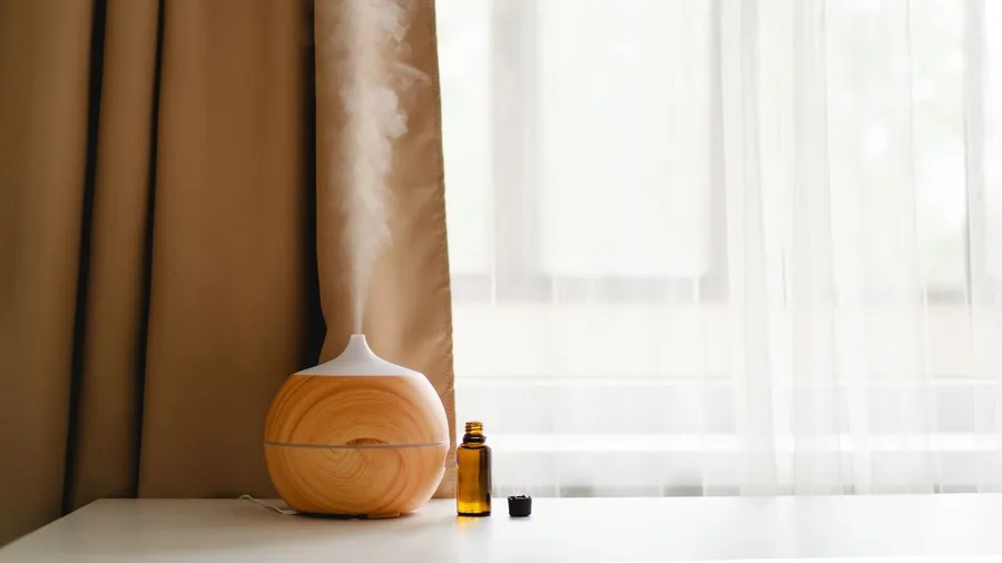 An essential oil diffuser emitting mist next to a bottle of oil in a serene setting.
