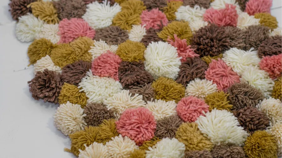 A handmade colorful pom-pom rug on a white surface.