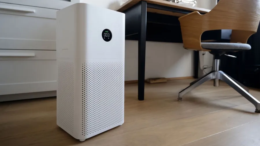 A smart air purifier near a table and chair on a wooden floor.