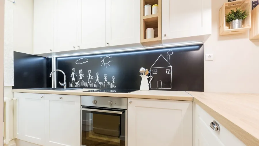 A kitchen interior with white cabinets, wooden countertop, and a chalkboard backsplash.