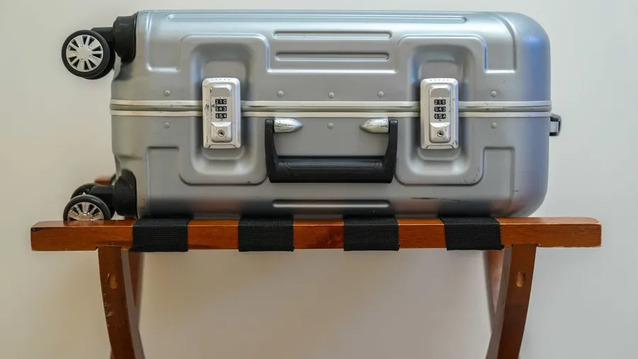 A wooden luggage rack with a silver suitcase on it.