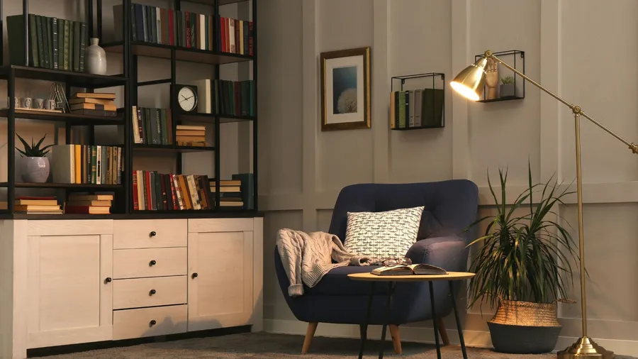 A cozy reading nook featuring a comfortable chair, a warm blanket, a stylish lamp, and a well-organized bookshelf filled with books and decor accents.