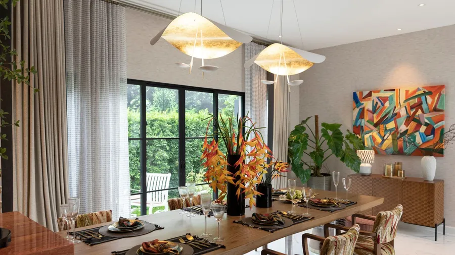 An inviting dining area featuring a beautifully set table with vibrant floral arrangements, modern artwork, and ample natural light from large windows.