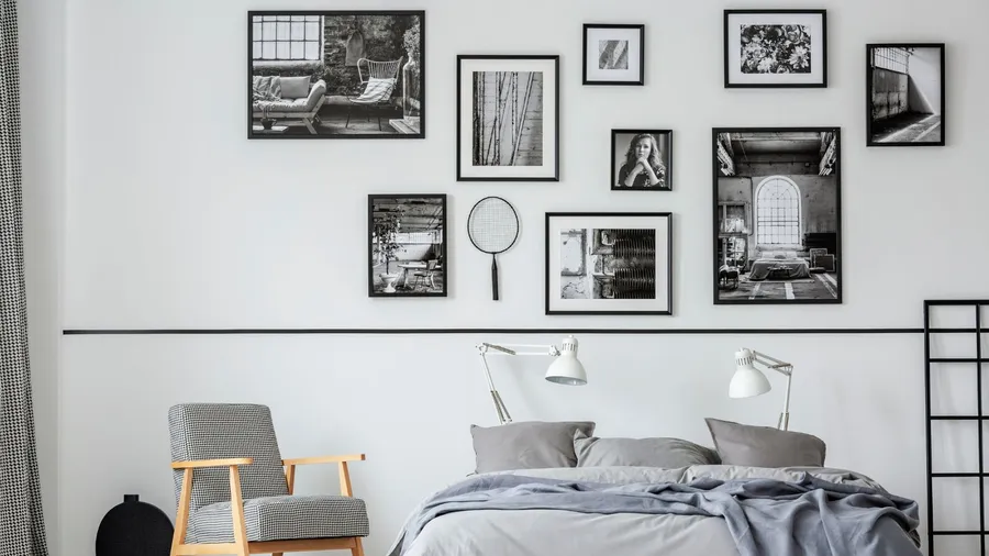 A stylish bedroom interior with a cozy bed, wooden armchair, lamps, and a monochromatic gallery wall.