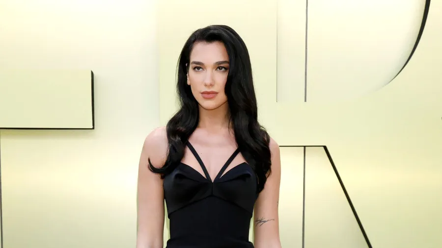 Singer Dua Lipa wearing a beautiful black dress and posing at an event.