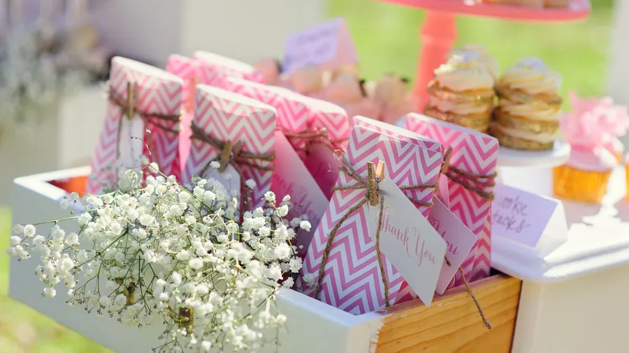 Party favors with a small thank you note arranged in a wooden tray with flowers.