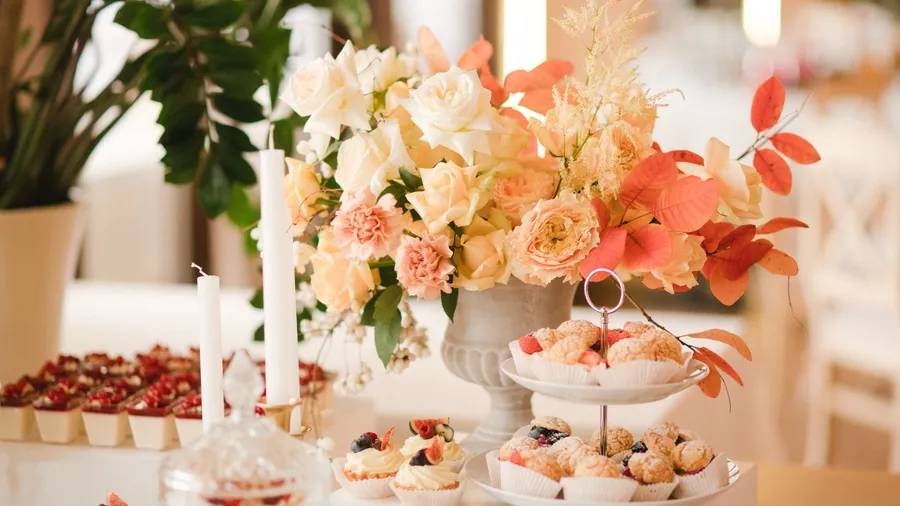 A beautiful dessert table setting with fresh flowers arranged in a vase, candles and sweet treats.