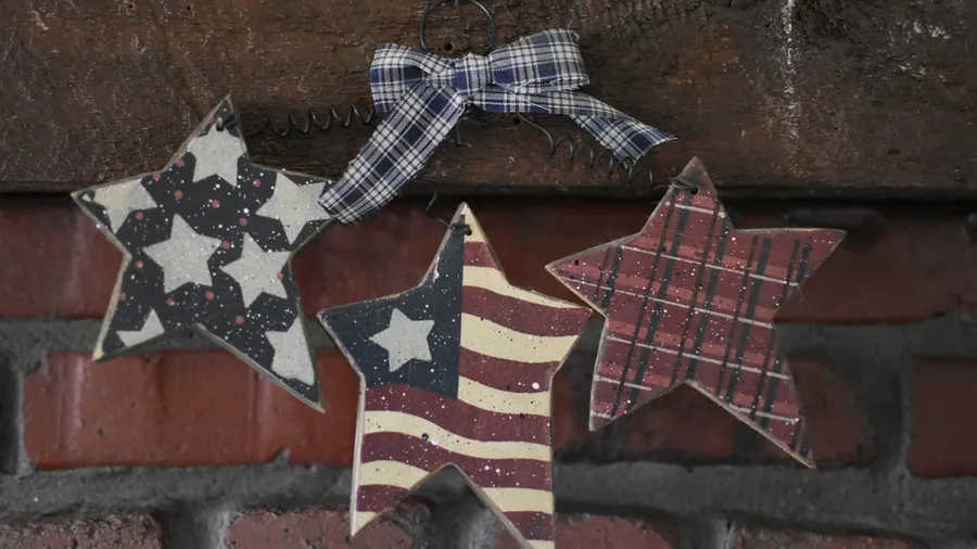 Wooden starts hanging on a brick wall with stars, checkered patterns, and USA flag painted on them.