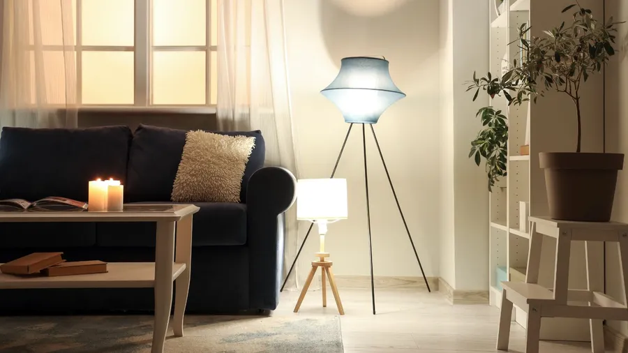 A living room interior with a blue sofa, throw pillow, coffee table with burning candles and books, houseplant, and floor lamps of different lengths.