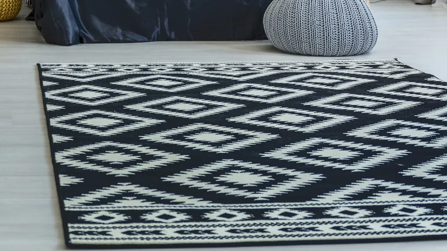 A gray pouf and a monochromatic rug on the floor.