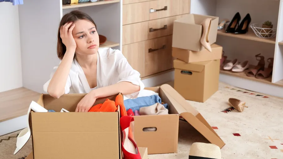 A lady looking upset while decluttering the wardrobe with storage boxes in front of her.