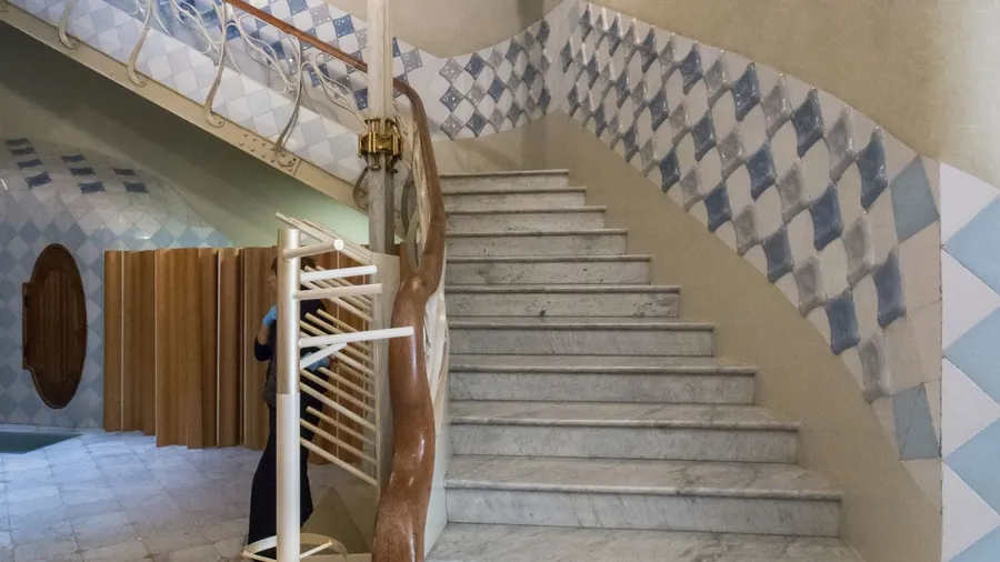 Interior staircase features smooth marble steps, a twisted wood-and-iron handrail, and walls adorned with glossy blue and white diamond-patterned ceramic tiles