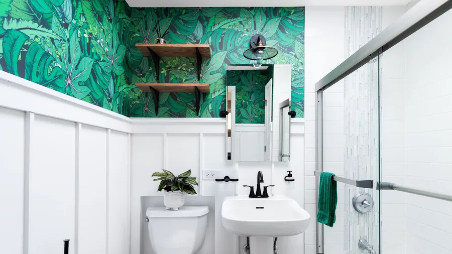 A bright white bathroom with a beautiful, colorful green leaf wallpaper.