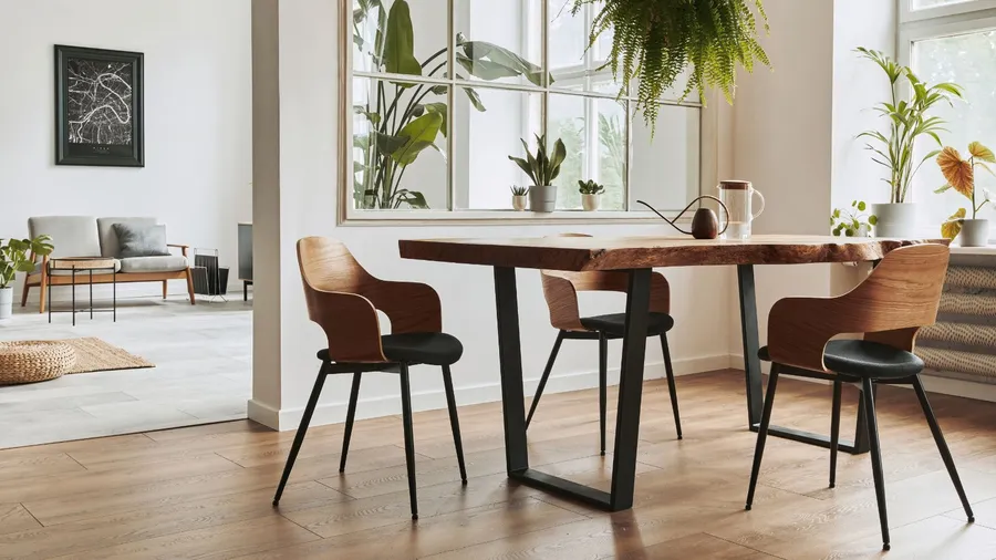 A dining area with a rustic wooden table, stylish chairs, and abundant natural light from large windows.