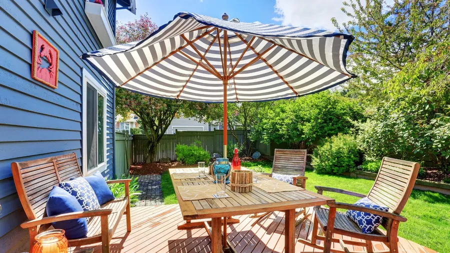 A stylish patio with a wooden table, chairs, throw pillows, and a striped patio umbrella.