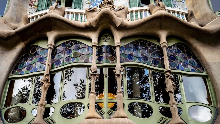 Architectural detail of Casa Batlló in Barcelona, showcasing unique organic shapes, colorful stained glass windows, and intricate stonework.