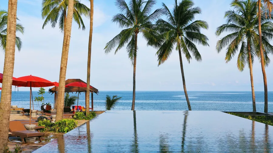 Swimming pool on the beach of Koh Samui. Beach pavilion with red roofs, palm trees and the tourist having a rest on pool side
