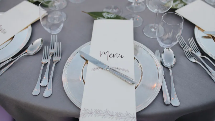 A table with gray tablecloth, stylish dinnerware, and a menu card placed on each plate.