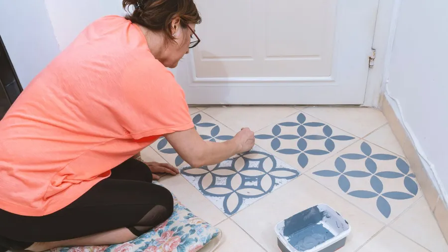 A woman painting floor tiles in a blue generic Turkish design.