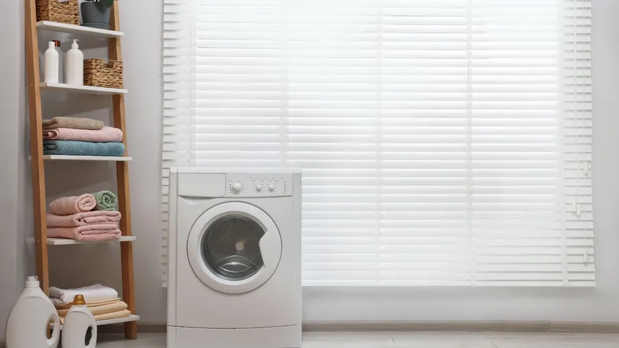 Laundry room with washing machine and towels on a shelf.