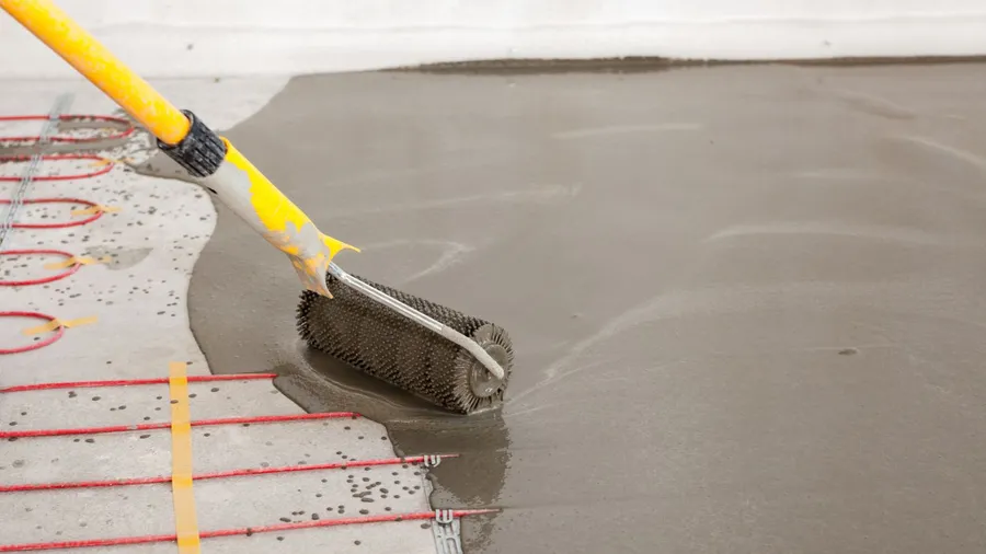 Worker using a spiked roller to smooth wet concrete over a radiant floor heating system.