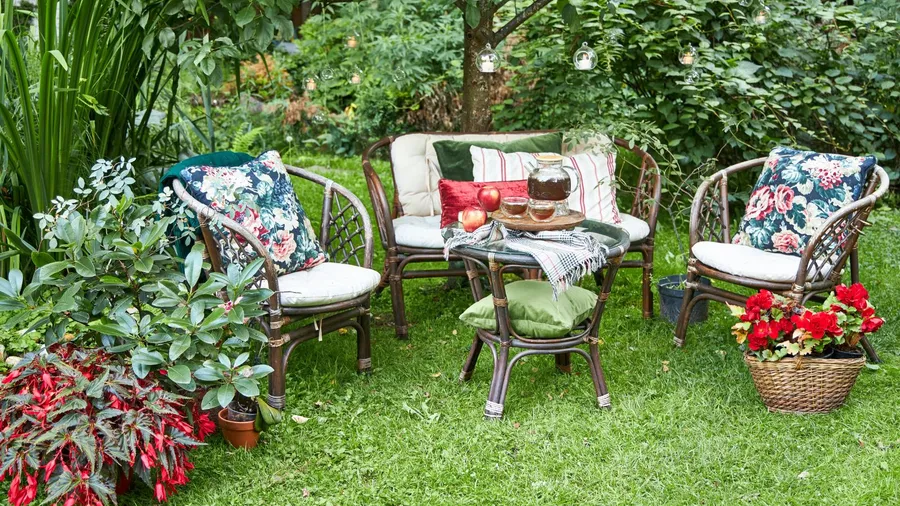 A garden with wooden sofas, table, throw pillows, and snacks surrounded by greenery.