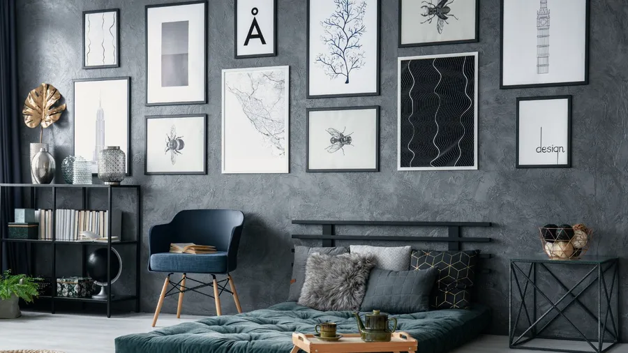 A modern bedroom interior with a blue armchair, green futon, personalized gallery wall on a textured limewash-painted wall, and a black bookcase with books and decorative accents.