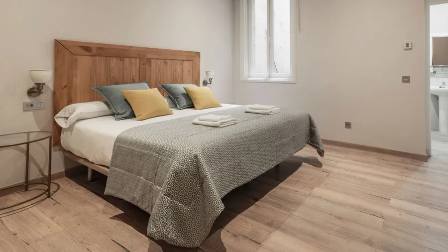 A bedroom interior with a bedside table, lamps, and a bed with a diy door headboard on the wooden floor.