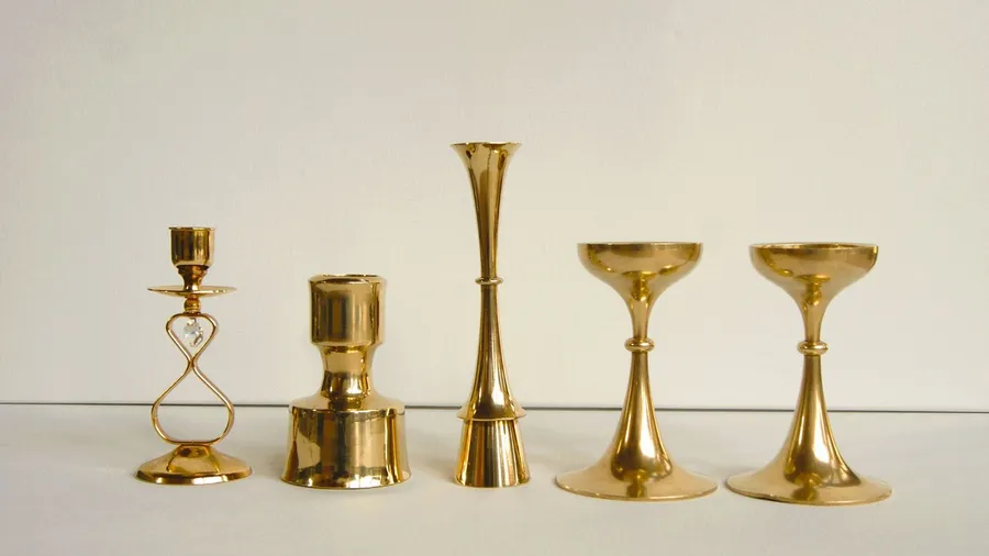 Golden decorative candle holders on a white table in front of a white wall.