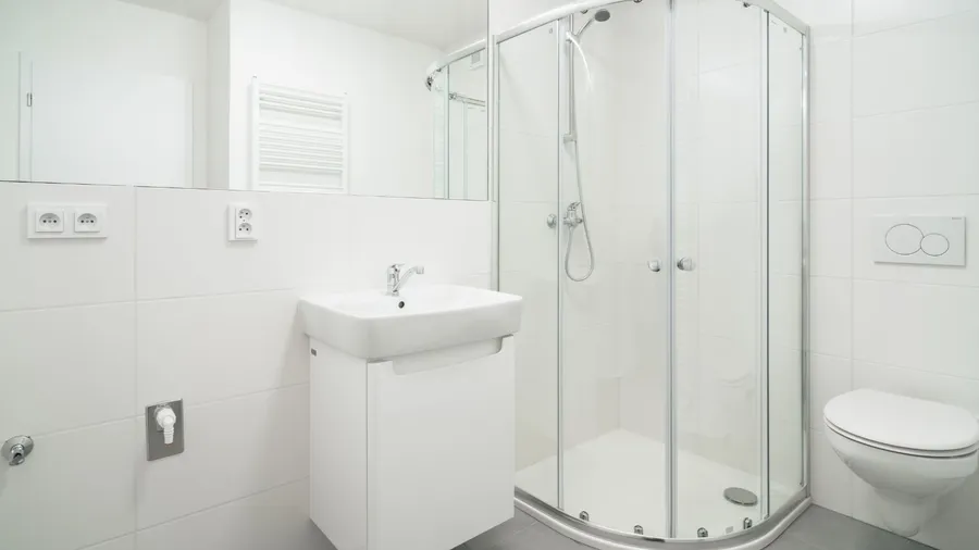 A bathroom interior with a large mirror, frameless glass shower, and large format tiles on the walls.