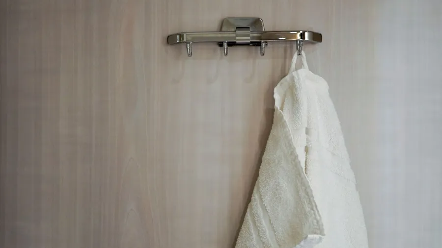 A towel hanging on a chrome hook attached on a wooden door.