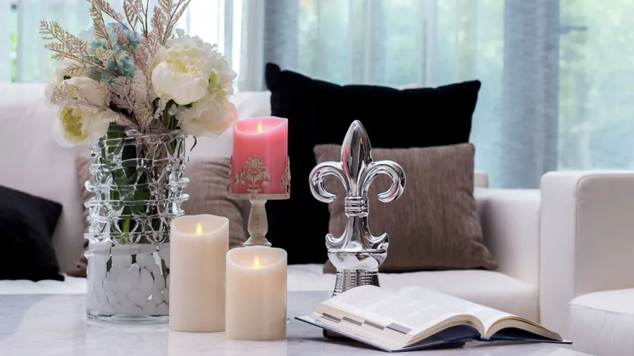 A decorative flower vase, candles, books, and decor accents on a coffee table.