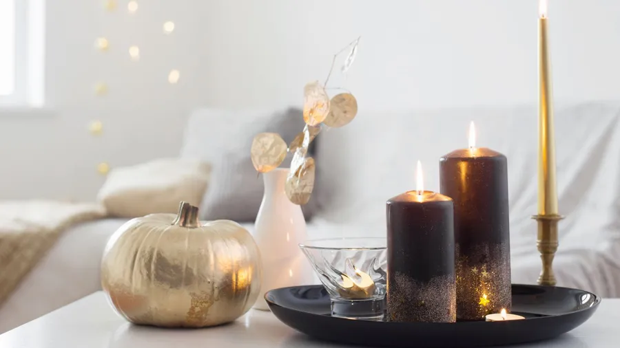 A white coffee table with dried leaves in a vase, metallic pumpkin, and candles in a decorative tray.