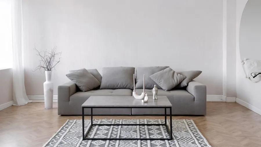 A stylish living room interior with a gray sofa, dried branches in vase, rug, and a stylish coffee table with sculptures on it.