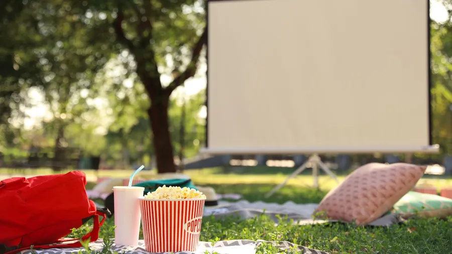 An outdoor theater setup with a projector, throw pillows, and snacks.