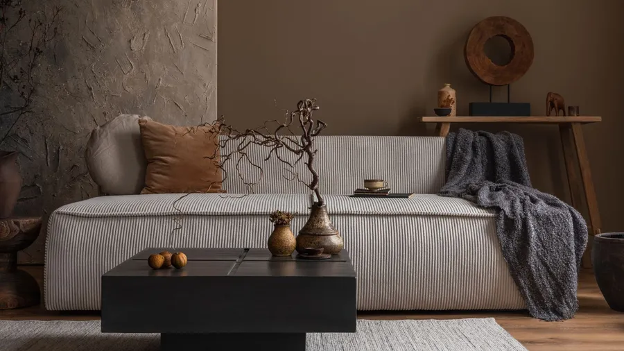A neutral living room interior with a cozy sofa, throw blanket, pillow, a wooden console table, and a coffee table with dried branches in a decorative vase.