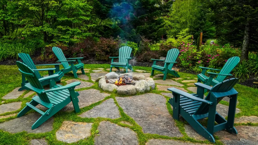 A beautiful garden with fire pit surrounded by adirondack chairs.