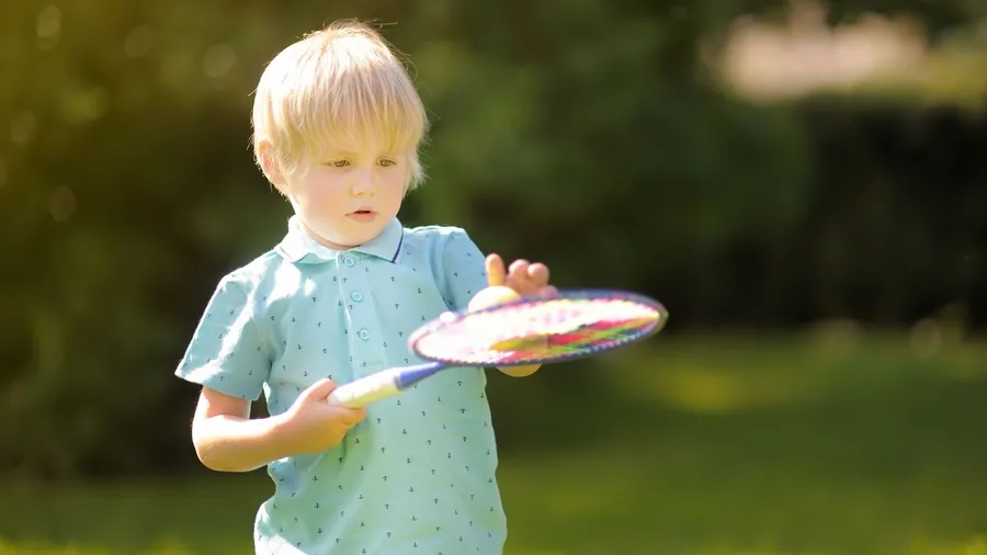 A young boy in a light blue shirt playing with a colorful spinning toy in a grassy outdoor area.