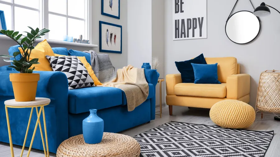 A stylish living room interior with a royal blue sofa, a yellow armchair, bold geometric accents, throw blanket and pillows, and a mirror on the wall.