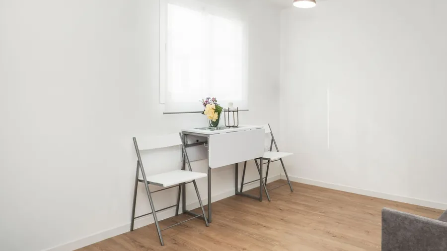 Foldable chairs and a drop leaf table near a window in a small living room.
