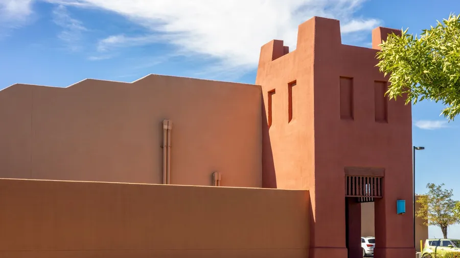 An adobe-style building with a warm, reddish-brown stucco exterior under a bright blue sky with white clouds.
